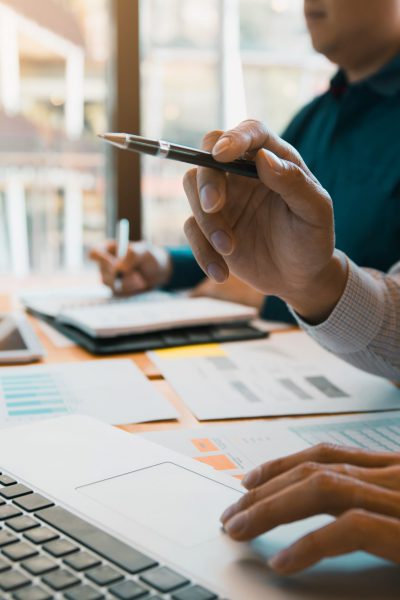 Business partnership pointing to the graph of the company financial statements report and profits earned during in the computer screen with giving a presentation to colleagues in office room.