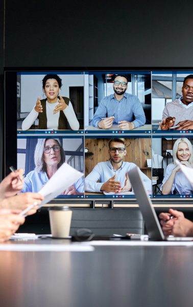 Global corporate video call in meeting room with diverse multiethnic people. Global corporation online videoconference in meeting room with diverse people sitting in modern office and multicultural multiethnic colleagues on big screen monitor. Business technologies concept.